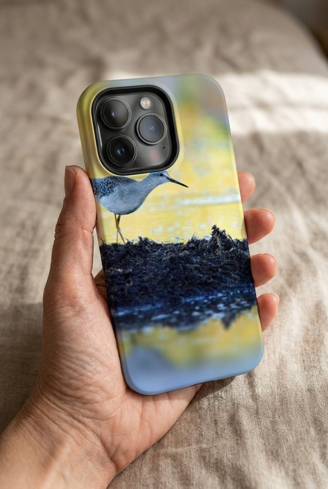 Hand holding an iPhone 17 Pro in a custom Tough case printed with a small shorebird on dark rocks, the bird placed below the camera.